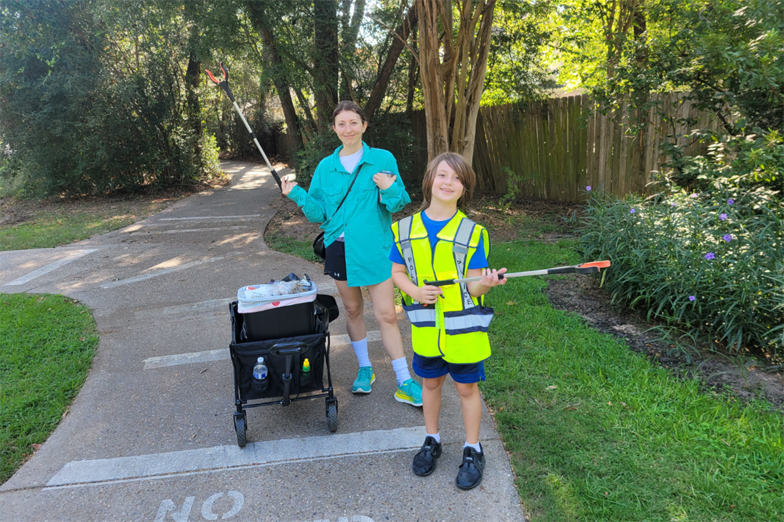 Photo of two smiling people on a trail holding trash grabbers