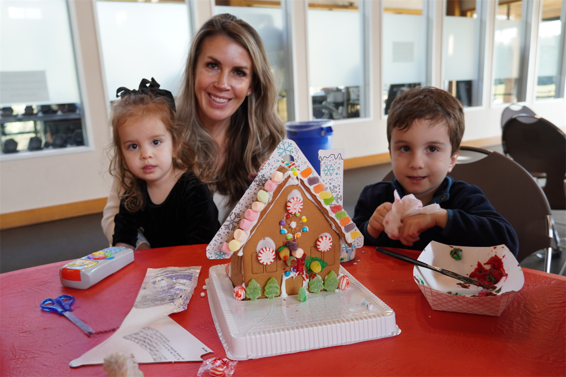 Photo of smiling parent and children holding gingerbread house