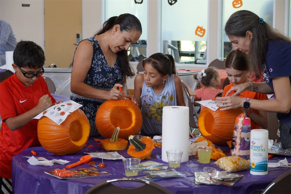 Photo of adults and children carving large orange pumpkins on a table