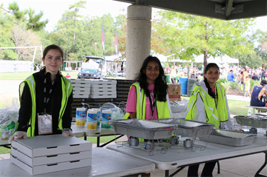 Photo of three smiling volunteers wearing green vests serving food