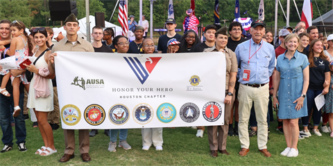 Group of people standing outside holding a large military banner