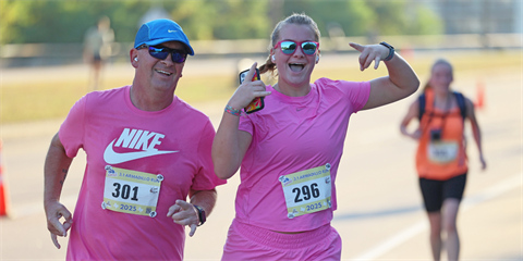 Two smiling people wearing pink running.