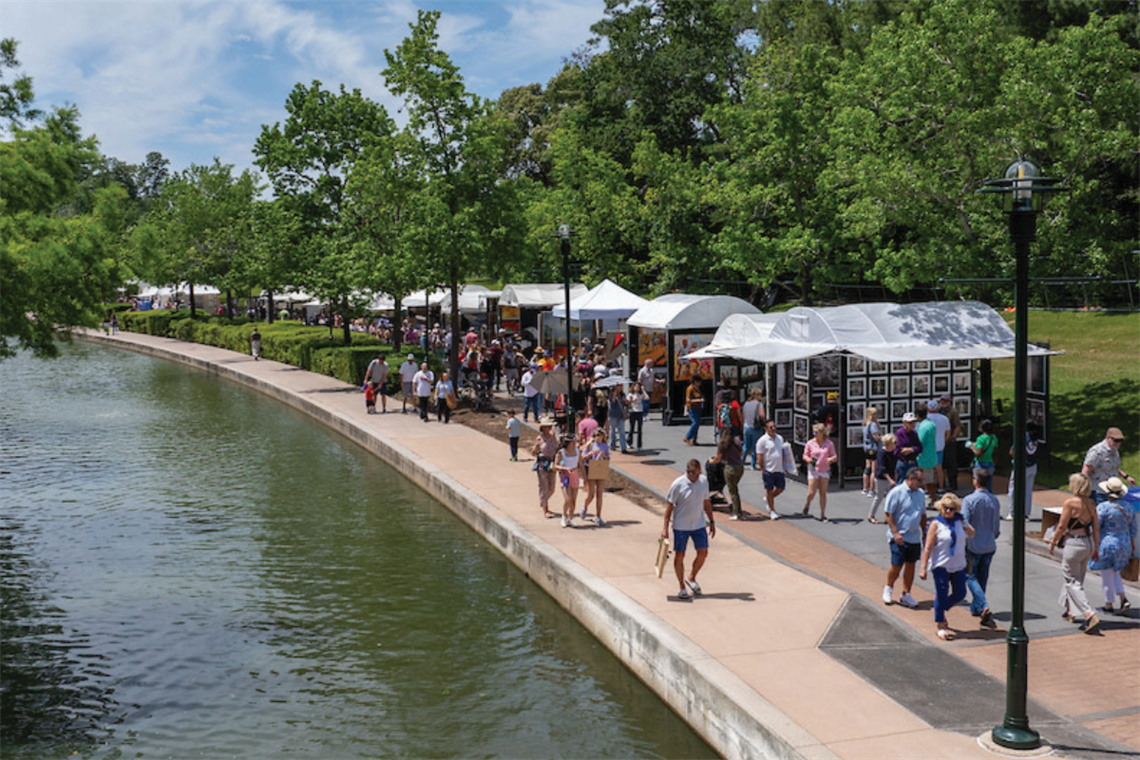People walking along a tree-lined sidewalk near a water canal