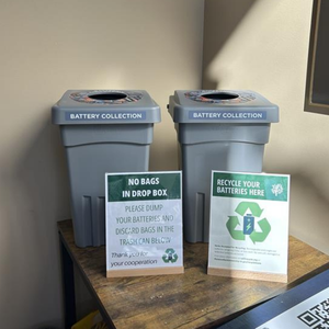 Two battery collection bins on a table with battery recycling signs
