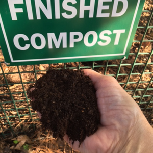 Person holding a finished compost sample in front of a compost bin