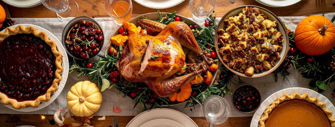 A spread on a table featuring a turkey roast, stuffing, pies, cherries and pumpkins