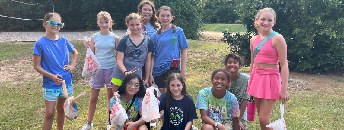 A group of young people holding up grocery bags filled with trash outdoors