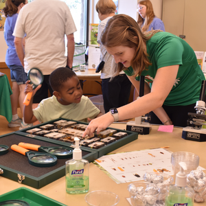 Woman assisting a young boy with using a magnifying glass to look at insects