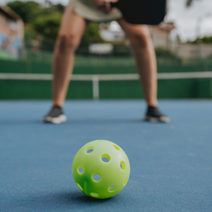 Pickleball on the ground of a court with a player out of focus in the background