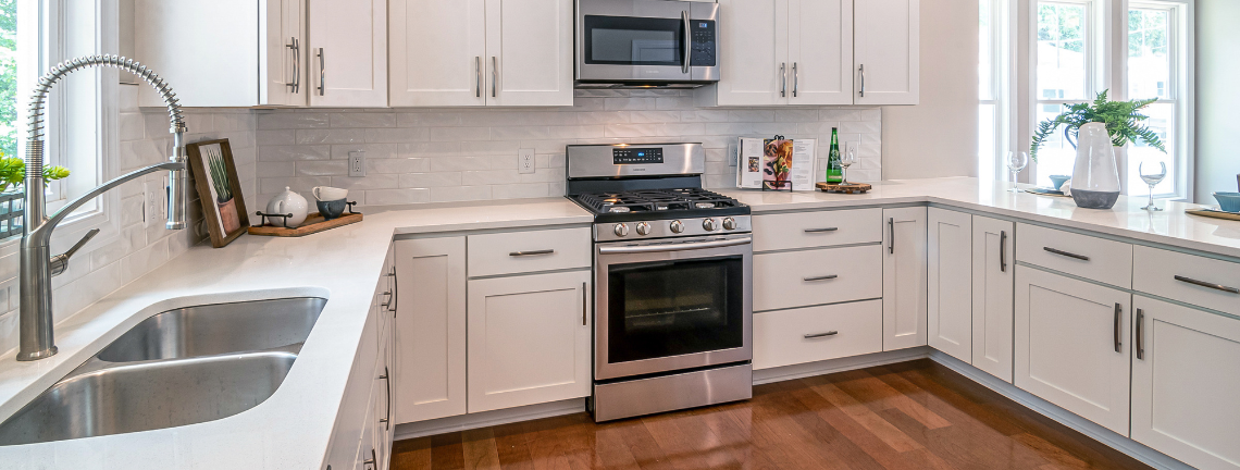 A view of a kitchen with white cabinetry, a sink, stove and microwave