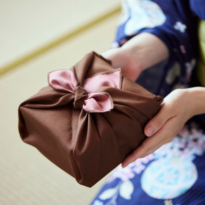 Person holding a gift wrapped with brown and pink fabric