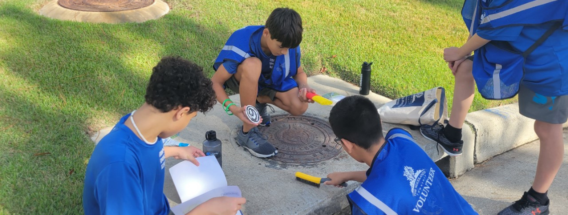Young men preparing a storm drain for placement of a marker