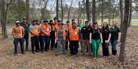 Smiling people wearing orange vests and company shirts standing in a forest