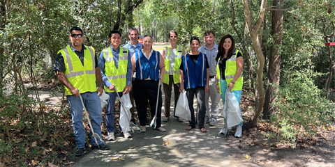 Photo of a group of smiling people standing on a pathway wearing safety vests and holding trash grabbers