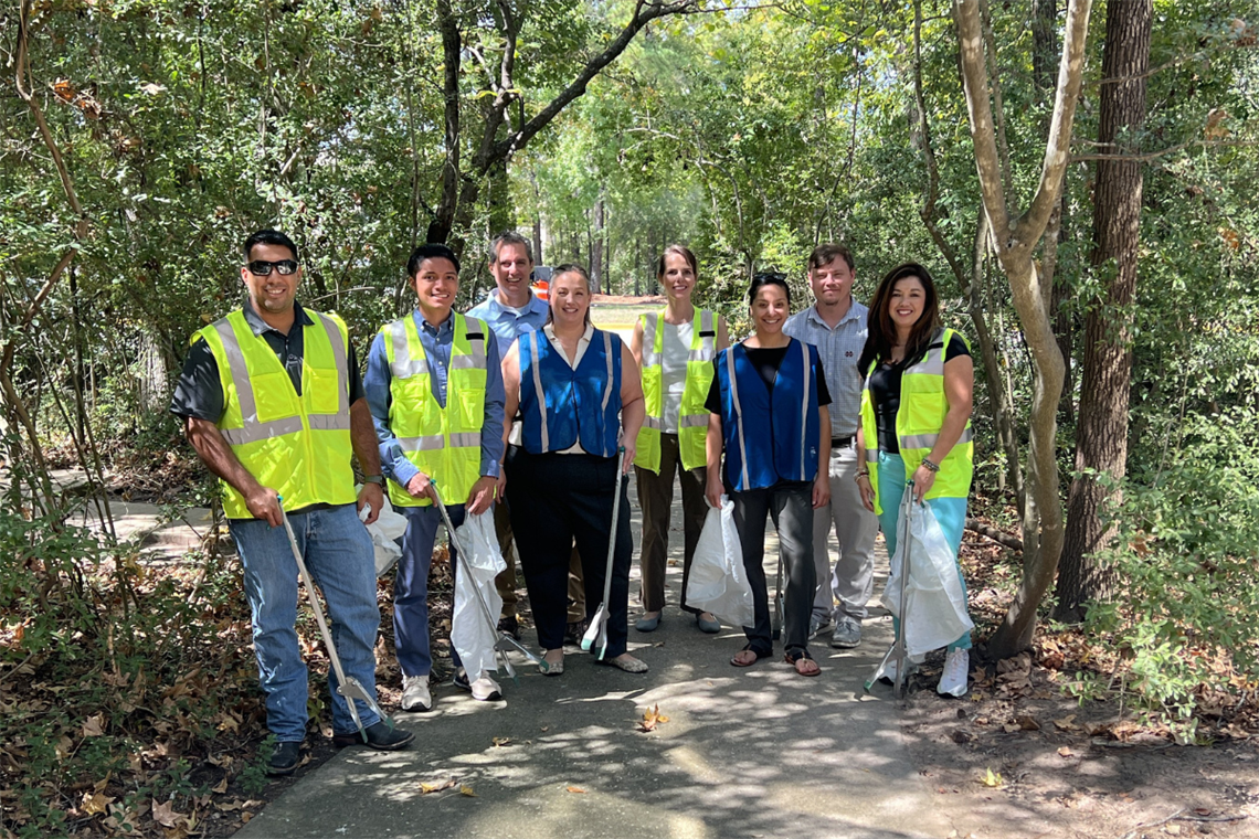 Smiling group of volunteers wearing yellow safety vest helping to clean a pathway in the woods