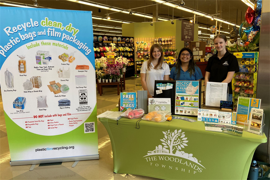 Photo of 3 smiling people standing behind a table with recycling information