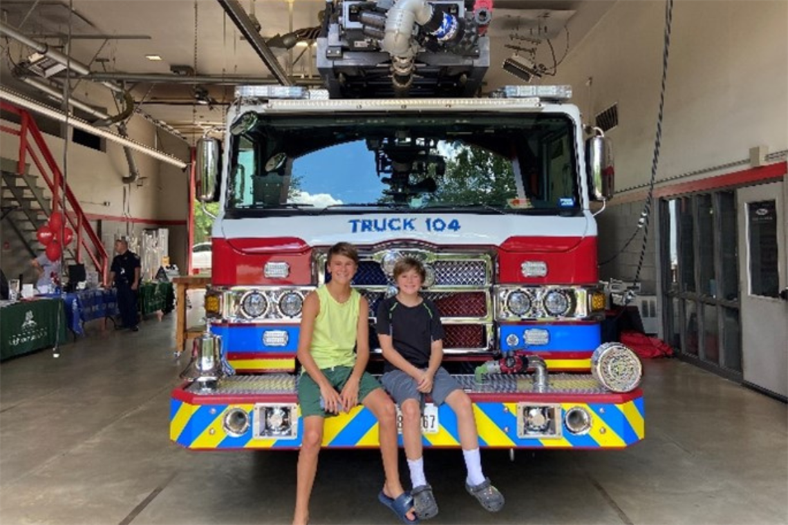 Photo of two smiling boys sitting on the front of a fire truck