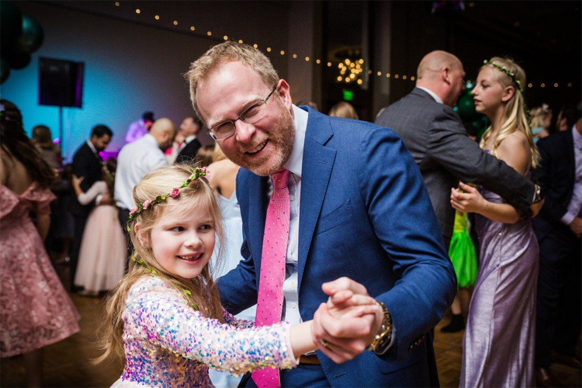 Photo of a father and daughter smiling at the camera while holding hands