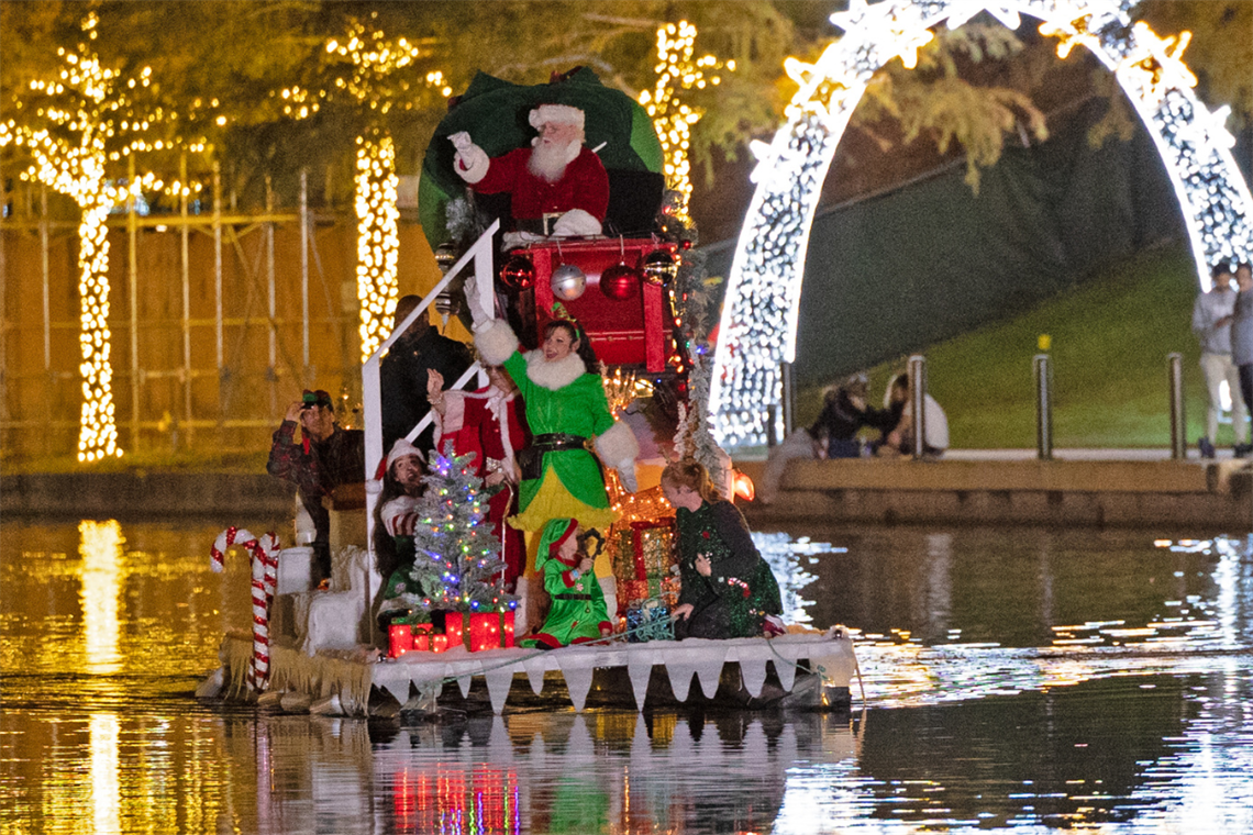 Photo of Santa Claus and an elf dressed in green waving to the crowd on a boat