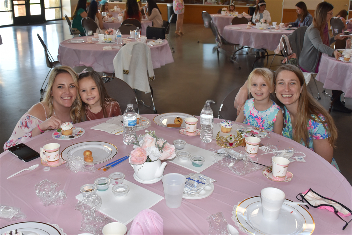 Photo of a pair of moms and daughters sitting at a pink table