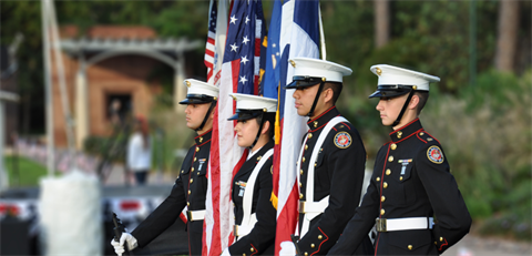 Photo of four people in blue military uniforms standing with the American flag.
