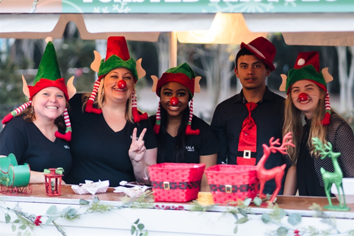 Photo of three smiling people with red and green elf hats on
