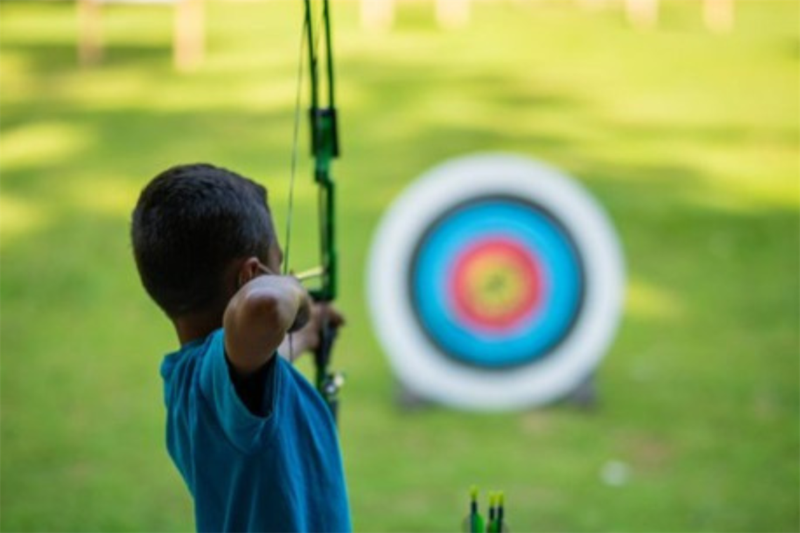Photo of a young person aiming a bow and arrow at a blue and red target circle