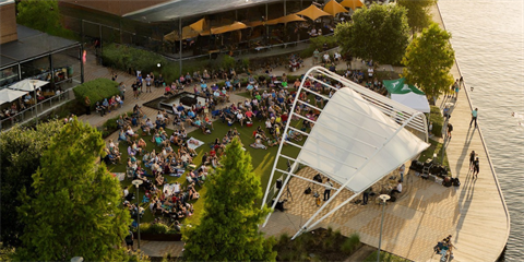 An arial view of a band on stage and concert goers sitting on the green lawn in front of the stage